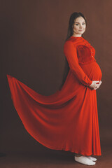 Naklejka premium Pregnant woman in red flying dress holding her belly.