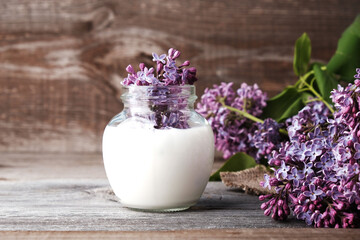 Natural cosmetics concept, skin and body care, lilac flowers in  jar with milk on wooden background with copy space