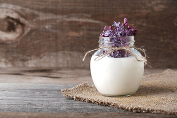 Lilac flowers in  jar with milk on wooden background with copy space. Natural cosmetics concept, skin and body care, aromatherapy and herbal medicine