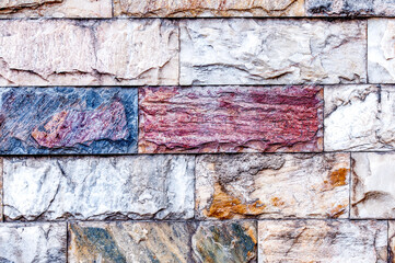 The wall is made of textured marble of different colors. A stone wall with an interesting marble texture. The marble facing of the wall.