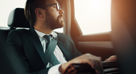 Thoughtful businessman in formal suit traveling in car on back seat looking outside the window