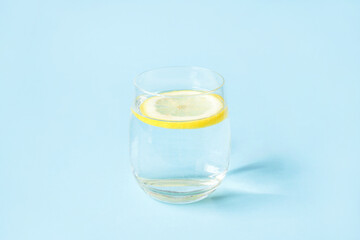 Glass of water with lemon on a blue background. Summer refreshing drink.