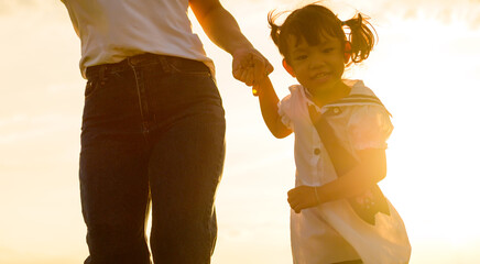 Silhouette of little girl holding parent hand at sunset 