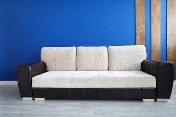 Fototapeta na wymiar Close-up of comfy sofa for office or living room. Stylish white colour and black insert. Bright blue wall with wooden decoration. Comfort and trendy interior design concept
