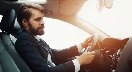 Side view of businessman sitting in car behind wheel looking at smartphone on dashboard and talking