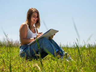 A beautiful female sketching on her notebook while sitting on a grass-covered field on a sunny day