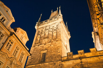 Look up the illuminated Lesser town tower of Charles bridge at twilight with its typical gothic...