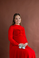 Beautiful pregnant woman holding baby booties, posing in the studio