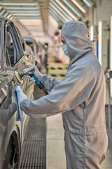 An employee of the car body paint shop with a medical mask on his face polishes the painted surface