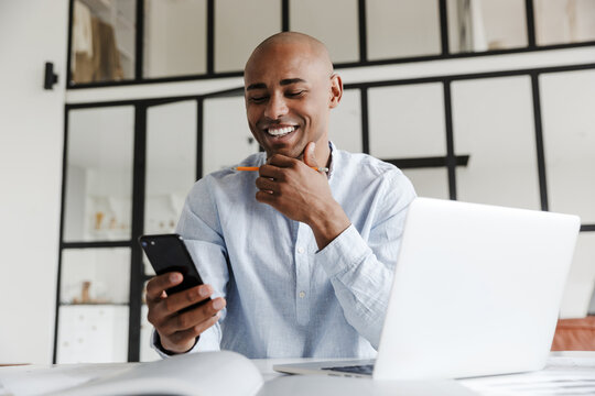 Photo of man using mobile phone while working with laptop