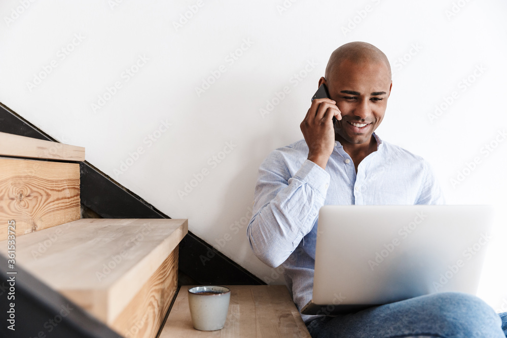 Wall mural Photo of african american man using laptop and talking on cellphone