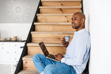 Photo of man using laptop and drinking coffee while sitting on stair