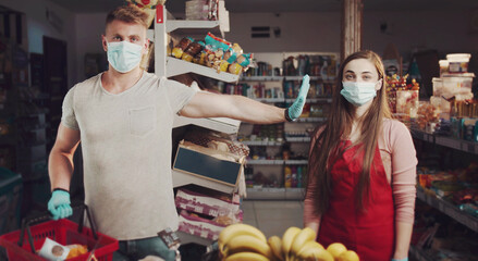 Casual guy in protective mask and gloves stretching arm out as stop sign towards girl shop assistant