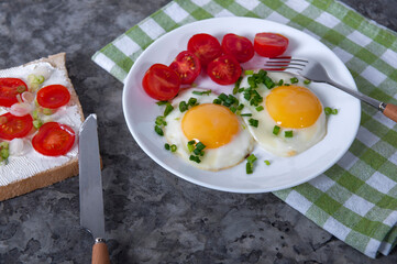 An appetizing breakfast with fried eggs, bread, cherry tomatoes and cheese. Fried eggs for breakfast. Sandwich with cheese and cherry tomatoes.
