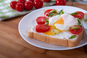 A delicious breakfast with poached egg, bread, cherry tomatoes, cheese and herbs. Poached egg for breakfast. Sandwich with cheese, red cherry tomatoes, herbs and poached egg.