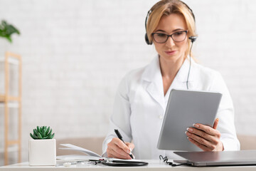 List of symptoms. Woman doctor with headphones holding tablet in hands