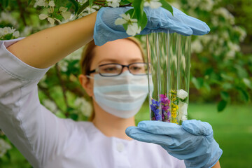 Female scientist wearing glasses, mask and gloves with test tubes in her hands studies the...