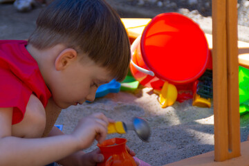 A boy is playing in the sandbox. Sunny summer, equip a place for games for a child in the yard. Happy kids at home