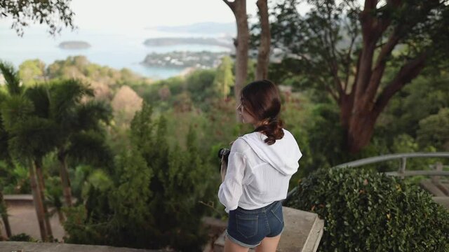Karon observation deck on the island of Phuket. among a large amount of greenery, a young girl stands with her back to the viewer, taking pictures of the sea view