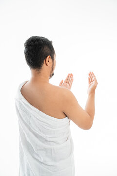 Muslim man praying while standing in white traditional clothes open his arm shoot from behind