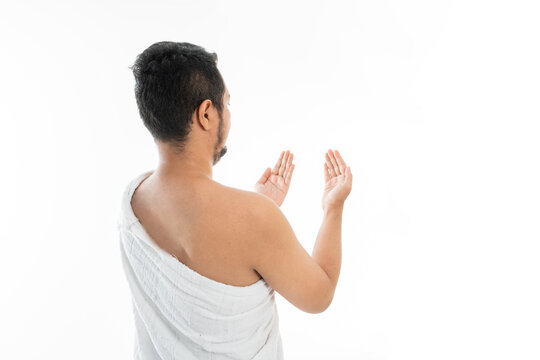 Muslim man praying while standing in white traditional clothes open his arm shoot from behind