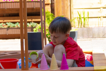 A boy in a red T-shirt playing in the sandbox. Summer sunny day at home