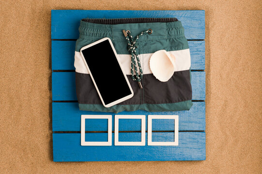 blue wood and sea sand swimsuit with black screen smartphone and white shell on top.mockups photo Top view