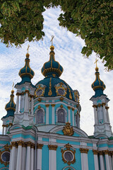 Fototapeta na wymiar Picturesque landscape view of famous Saint Andrew?s Church in tree Leaves border. colorful vibrant sky with soft clouds in the background. Touristic place and romantic travel destination in Kyiv