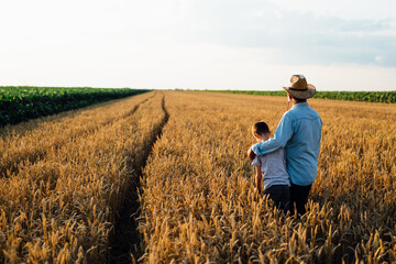 Naklejka na ściany i meble man holding his grandson standing in wheat field