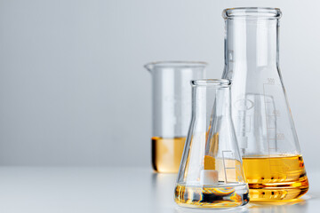 Laboratory glassware with yellow oily liquid on grey background