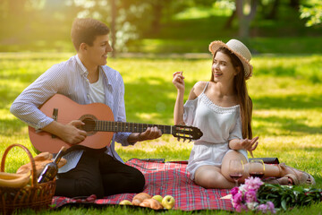 Affectionate boyfriend playing guitar and singing song for his girlfriend during summer picnic at park