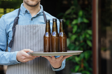 Barman in apron carries tray with bottles of beer in bar