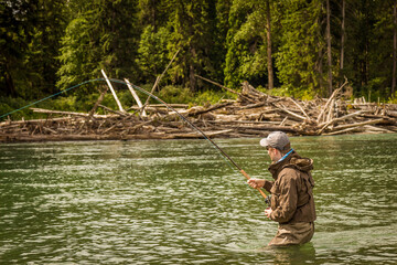 A man hooked into a fish while fly fishing on a deep green river.