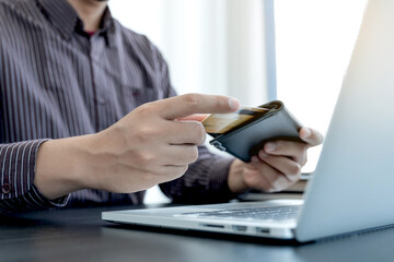 Fototapeta premium The businessman's hand is holding a credit card and using a laptop for online shopping and internet payment in the office