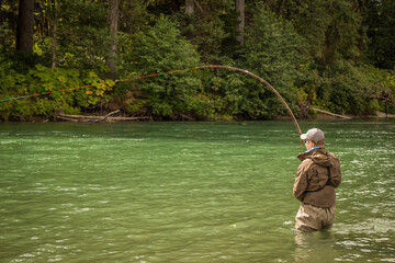 A man hooked into a fish while fly fishing on a deep green river.