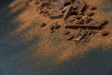 Dark chocolate stack, chips and cocoa powder with coffee beans on a dark background. Confectionery and food concept. Top view, copy space, selective focus.