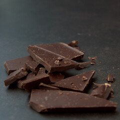 Dark chocolate stack, chips and cocoa powder on a dark background. Confectionery and food concept. Top view, copy space, selective focus.