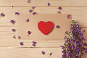 red wooden small heart brown envelope on wooden table with bouquet of flowers lupine lies on brown envelope on wooden table diagonally