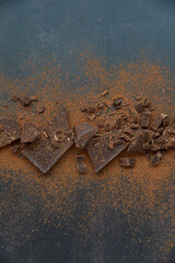 Dark chocolate stack, chips and cocoa powder on a dark background. Confectionery and food concept. Top view, copy space, selective focus.