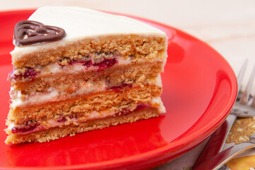 Slice of white cake with four layers on a red plate with chocolate shapes decoration