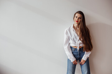 Portrait of a beautiful girl rejoicing life standing against the wall in a white shirt