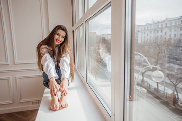 beautiful girl sitting on the window and smiling