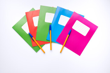 Colorful school exercise books and writing pens on white background.