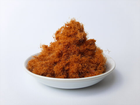 Chicken floss, is a dried meat product with a light and fluffy texture similar to coarse cotton. On a small plate, isolated in white background