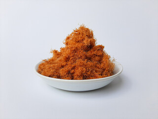 Chicken floss, is a dried meat product with a light and fluffy texture similar to coarse cotton. On a small plate, isolated in white background