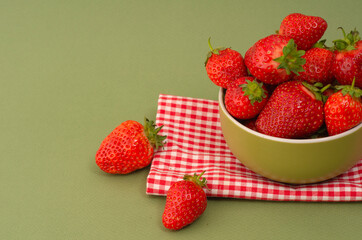 Fresh red strawberries in a bowl on green background and towel