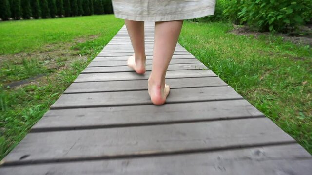 Barefooted female legs on a wooden path (flooring) in a park (forest). Summer walk in nature. Rest, relaxation, health, walk concept.