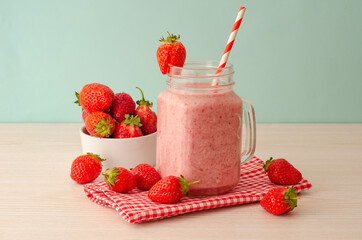 Strawberry smoothie or milkshake in mason jar on 
light wood table. Healthy food for breakfast and snack.