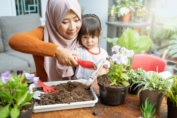 Asian mother helps her daughter hold a small shovel filled with soil to grow potted plants as a home activity