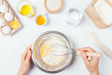 Female hands whisk flour and eggs in metal bowl to cook dough for homemade bread